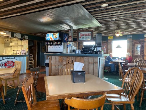 Interior of a rustic restaurant with wooden decor, a counter, and patrons dining at tables.