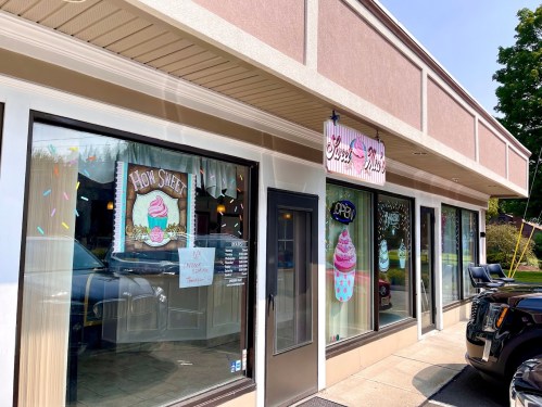Exterior of a colorful ice cream shop with large windows displaying "How Sweet" and "Open" signs.