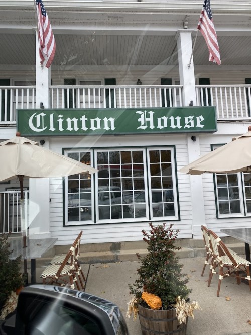 Sign for "Clinton House" on a white building, with American flags and outdoor seating visible.