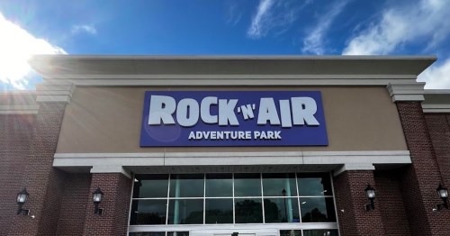 Sign for "Rock 'n' Air Adventure Park" on a building with a blue sky and clouds in the background.