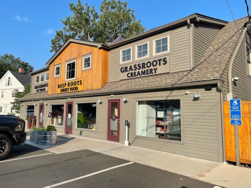 Exterior of a building featuring "Grassroots Creamery" and "Deer Roots Street Food" signs, with a clear blue sky above.