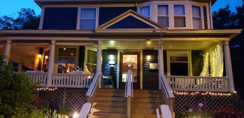 A charming two-story house at night, illuminated with warm lights and surrounded by greenery.