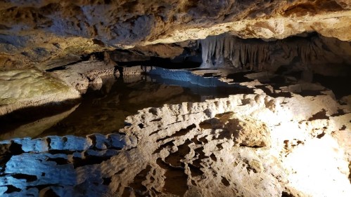 A dimly lit cave interior with rock formations and a reflective pool of water.