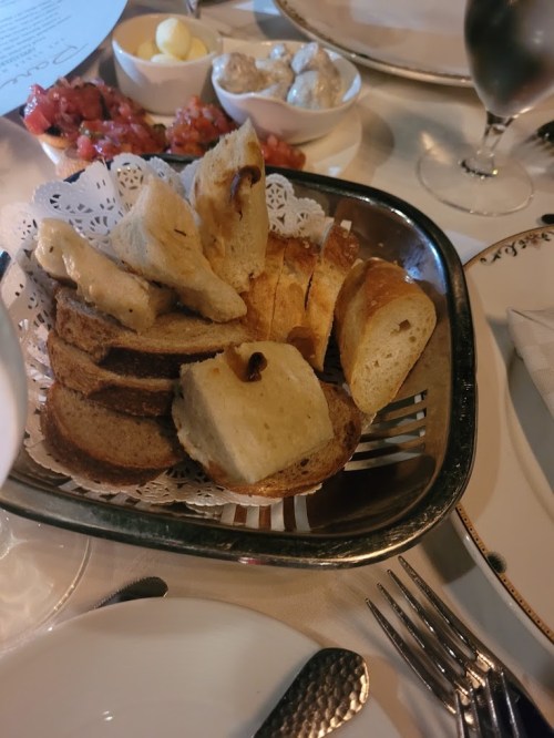 A basket of assorted breads, including slices of white and dark bread, served with butter and dips on a table.