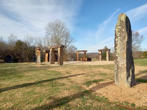 A stone monument with large upright stones and a grassy area under a blue sky with wispy clouds.