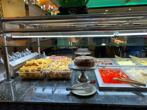 A buffet display featuring various desserts, including cakes, jellies, and pastries, under bright lighting.