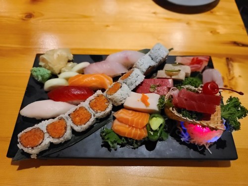 A colorful assortment of sushi and sashimi arranged on a black platter, garnished with wasabi and pickled ginger.