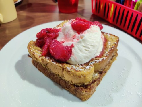 A slice of French toast topped with whipped cream and fresh strawberries, served on a white plate.