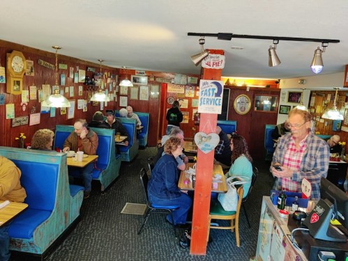 A cozy diner interior with blue booths, patrons enjoying meals, and vintage decor on the walls.