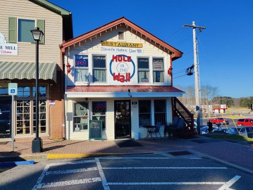 A quaint restaurant named "Hole in the Wall" with an open sign, located in a historic building on a sunny day.