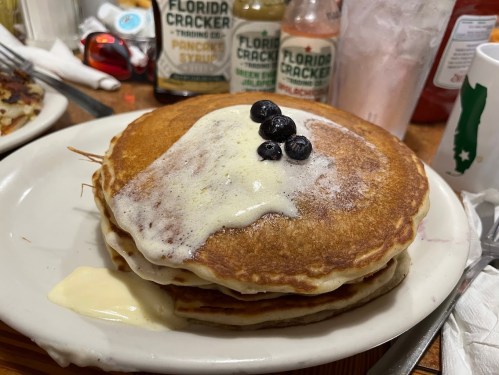 A stack of three pancakes topped with a dollop of cream and blueberries, served on a white plate.