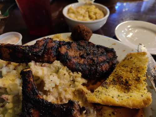 A plate of grilled pork chops with mashed potatoes, a piece of garlic bread, and a bowl of macaroni and cheese.