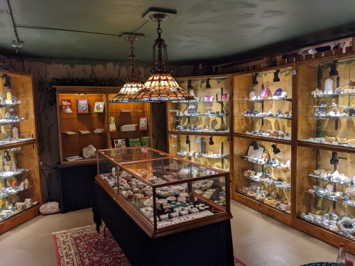 A cozy room filled with illuminated display cases showcasing various minerals and gemstones, with a central glass display.