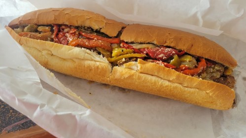 A sub sandwich filled with sliced meats, peppers, and onions, served in a toasted hoagie roll.
