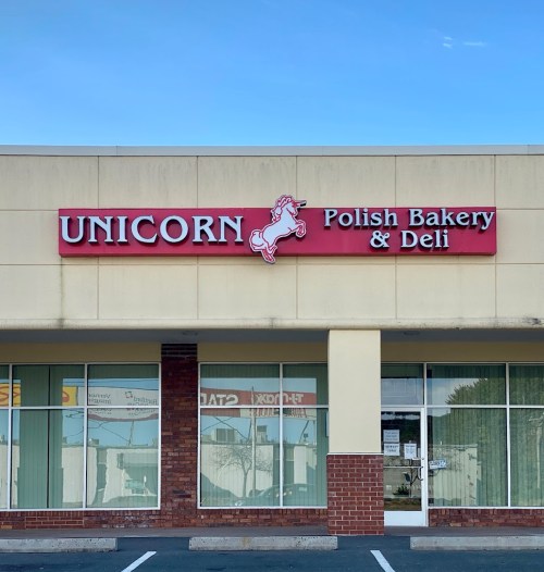 Sign for "Unicorn Polish Bakery & Deli" featuring a unicorn graphic, set against a light blue sky.