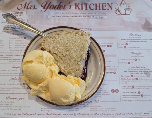 A slice of berry pie with a crumb topping served with a scoop of vanilla ice cream on a plate.