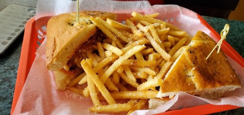 A sandwich with fries on a red tray, garnished with herbs and served with toothpicks.