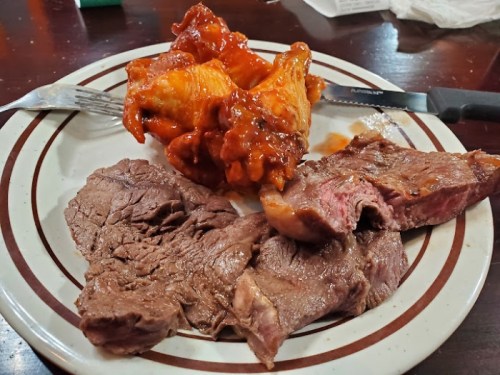 A plate with two slices of cooked beef and a portion of chicken wings in a spicy sauce.