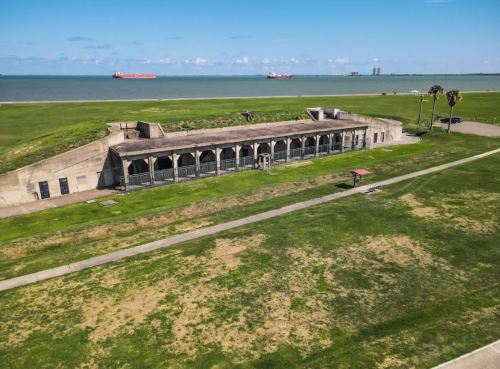 Aerial view of a historic fort structure near the water, surrounded by green grass and a clear blue sky.