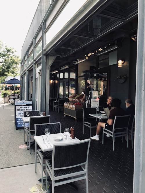 Outdoor dining area of a restaurant with tables set, a pickup sign, and patrons seated at a nearby table.