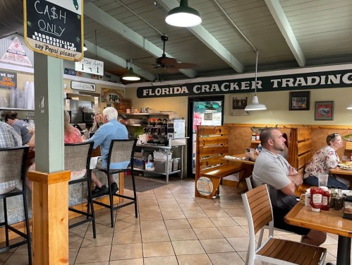 Interior of a casual restaurant with diners, a counter, and a sign reading "Florida Cracker Trading."