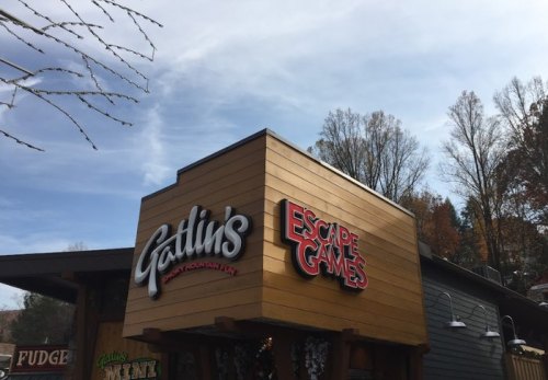 Sign for Gatlin's Escape Games, featuring a wooden exterior and a clear blue sky in the background.