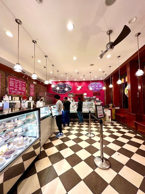 A cozy ice cream shop with a checkered floor, display cases, and customers ordering at the counter.
