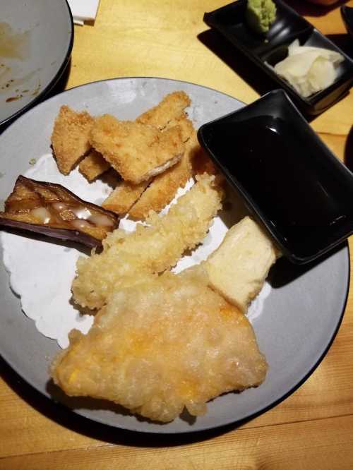 A plate with various fried foods, including fish, tofu, and a dipping sauce, accompanied by wasabi and pickled vegetables.