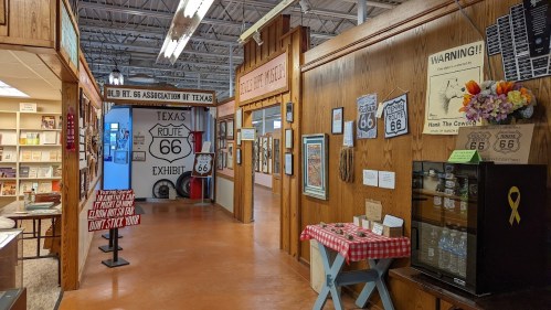 Interior view of a Route 66 exhibit featuring signs, artwork, and wooden walls in a museum setting.