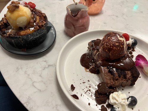 A dessert plate with chocolate cake topped with ice cream and chocolate sauce, alongside a bowl of warm dessert with ice cream.