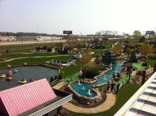 Aerial view of a mini-golf course with water features, greenery, and people enjoying the outdoor space.