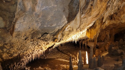 A dimly lit cave interior featuring stalactites hanging from the ceiling and stalagmites rising from the ground.