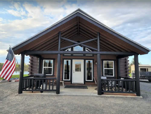 A log cabin-style building with a large front porch and an American flag, set against a cloudy sky.