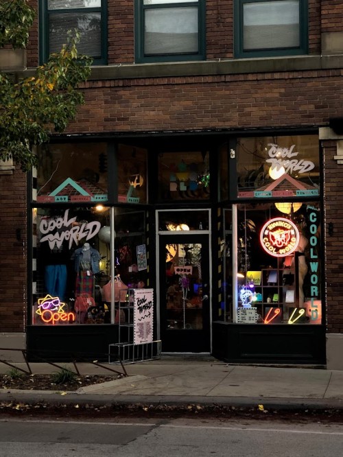 A storefront with neon signs reading "Cool World" and "Open," showcasing colorful merchandise in the windows.