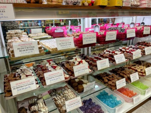 A display case filled with various homemade sweets, including cookies, candies, and desserts, with price signs.