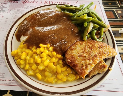 A plate of food featuring mashed potatoes with gravy, corn, green beans, and a breaded meat patty.
