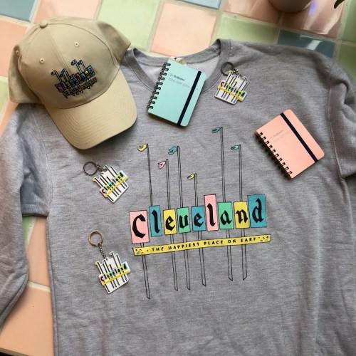 A flat lay of Cleveland-themed merchandise: a sweatshirt, cap, notebooks, and keychains in pastel colors.