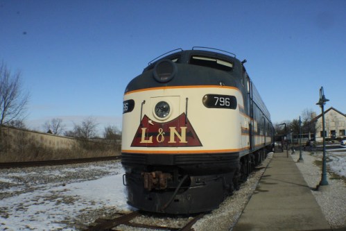 A vintage L&N train engine parked on a snowy track, with a clear blue sky in the background.