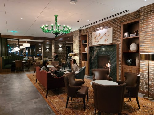 Cozy lounge with a fireplace, green chandelier, and guests relaxing in stylish seating around a coffee table.