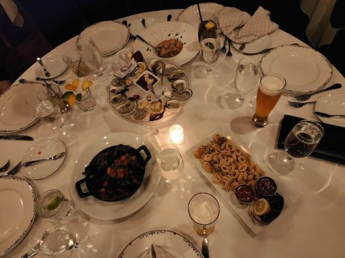 A beautifully set dining table with various seafood dishes, drinks, and a candle in the center.