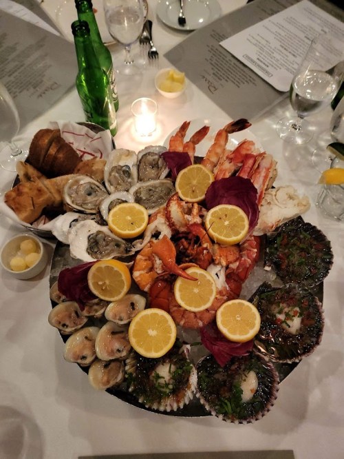 A large seafood platter featuring oysters, shrimp, lobster, and scallops, garnished with lemon slices.