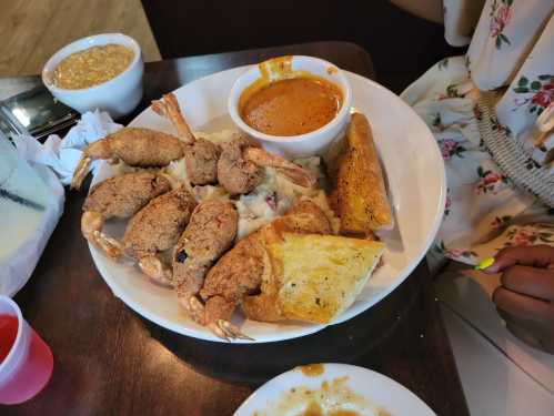 A plate of fried shrimp, mashed potatoes, a bowl of sauce, and garlic bread, served in a casual dining setting.