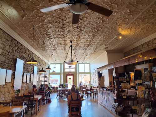 A cozy café with stone walls, wooden tables, and patrons enjoying their time, illuminated by natural light.