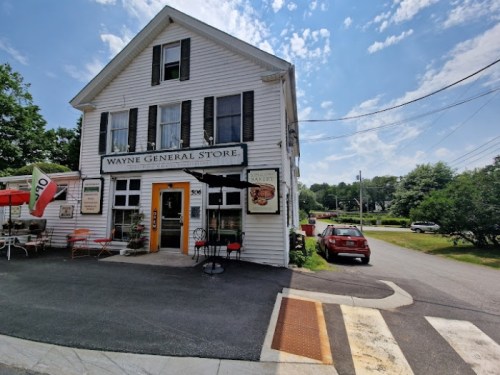 A white two-story building with a sign reading "Wayne General Store," surrounded by trees and a clear blue sky.