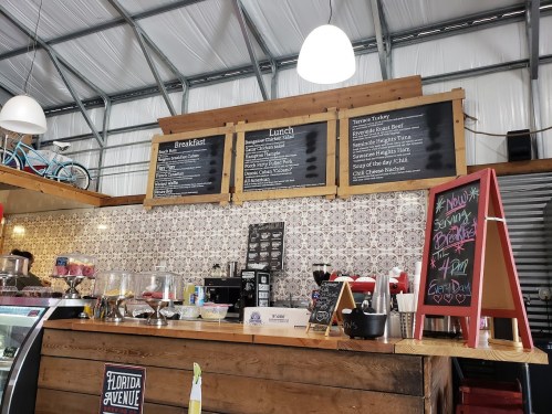 A cozy café interior featuring a wooden counter, menu boards, and a display of pastries and drinks.