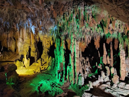 A colorful cave interior with stalactites and stalagmites illuminated in green and yellow light.