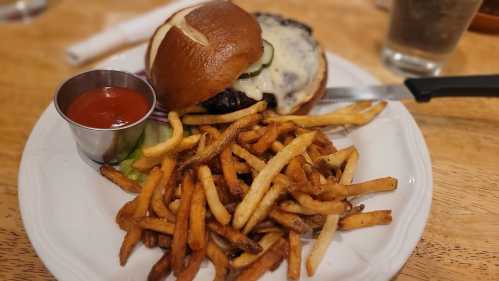 A juicy burger with cheese and pickles, served with a side of crispy fries and a small cup of ketchup.