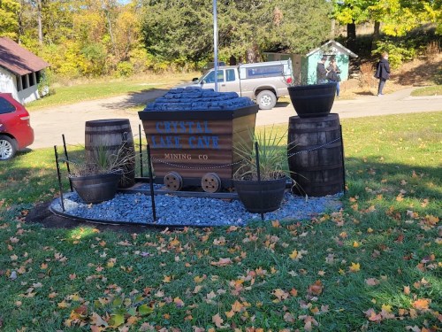 A decorative display featuring a wooden mining cart, barrels, and plants, set in a grassy area with autumn leaves.