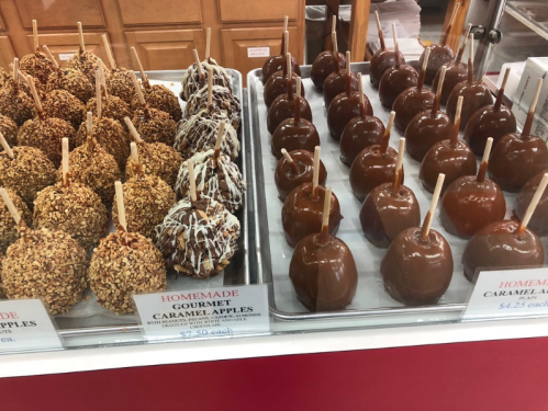 A display of gourmet caramel apples, some coated in nuts and chocolate, priced at $7.50 and $4.25 each.