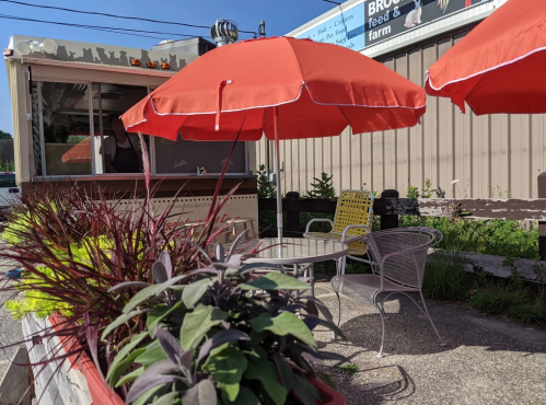 A food truck with red umbrellas and outdoor seating surrounded by plants and greenery.